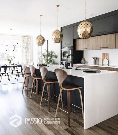 Réalisation de l'entreprise Ferland Drouin - Cuisine contemporaine avec îlot central blanc, tabourets en bois, armoires noires et en bois, et luminaires suspendus dorés, donnant sur une salle à manger lumineuse.