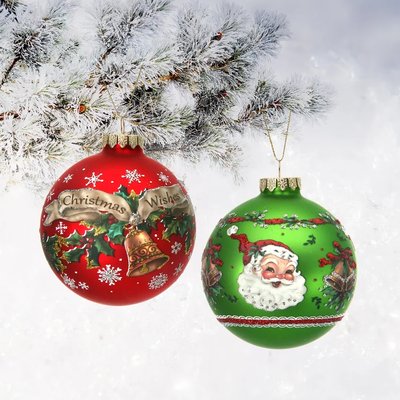 Deux boules de Noël décoratives accrochées à une branche enneigée. Une boule rouge ornée de houx, d'un message 'Christmas Wishes' et d'une cloche dorée, et une boule verte décorée avec un visage de Père Noël souriant, entouré de houx et de cloches.