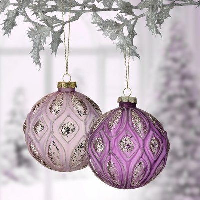 Deux boules de Noël suspendues, l'une rose pâle et l'autre violette, ornées de motifs scintillants en losanges et de détails élégants en relief. Elles sont accrochées à une branche décorative argentée avec un fond flou hivernal