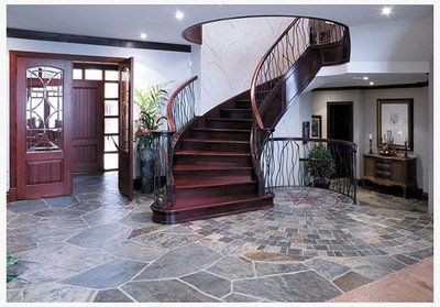 Entrée élégante avec un escalier en bois courbé et un plancher en ardoise aux teintes naturelles, ajoutant une touche rustique et raffinée à l'espace