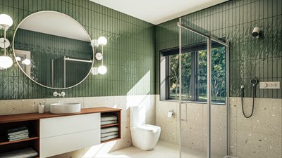 Salle de bain des enfants de la Maison Tanguay 2025, avec des murs en carreaux vert foncé, un bas de mur en terrazzo, un meuble-lavabo suspendu, un miroir rond, et une douche vitrée, baignée de lumière naturelle grâce à une grande fenêtre.