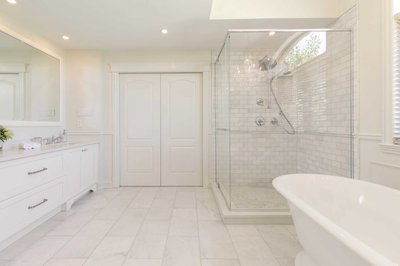 Salle de bain lumineuse avec meuble-lavabo blanc, grand miroir, douche vitrée avec carrelage en mosaïque, baignoire autoportante blanche et portes doubles blanches en arrière-plan.