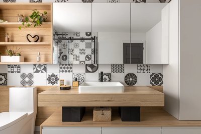 Vue de face de Salle de bain moderne avec carreaux à motifs noirs et blancs, douche vitrée à cadre noir, meuble-lavabo en bois clair avec vasque blanche, robinetterie noire, rangement mural en bois avec plantes décoratives, et fenêtre centrale laissant entrer la lumière naturelle.