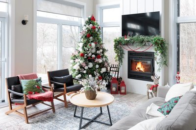 Salon vitré moderne décoré pour le temps des fêtes avec un sapin de Noël, une guirlande en haut d'un foyer et petites décorations de Noël un peu partout dans la pièce