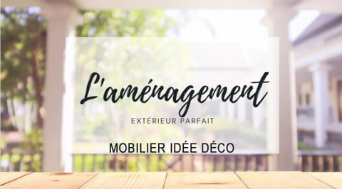 Une table en bois au premier plan avec, en arrière-plan, une terrasse lumineuse entourée de verdure. Sur l'image, le texte "L'aménagement extérieur parfait" et "Mobilier idée déco" est écrit en lettres noires élégantes, suggérant des conseils d'aménagement et de décoration pour l'espace extérieur.